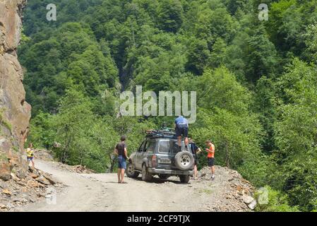 Omalo, Géorgie - 19 juillet 2017 : les voyageurs qui prennent des vélos sur le toit d'une voiture tout en se préparant à l'aventure sur la route de terre contre la forêt dense de feuillus à flanc de colline, le jour d'été ensoleillé Banque D'Images