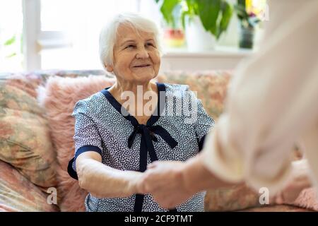 Femme soignant à domicile soutenant la vieille femme à se lever le canapé à la maison de soins Banque D'Images