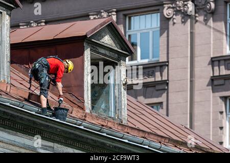 Riga, Lettonie- 3 juillet 2020: L'alpiniste industriel enlève les feuilles et la saleté de la gouttière de toit de maison Banque D'Images