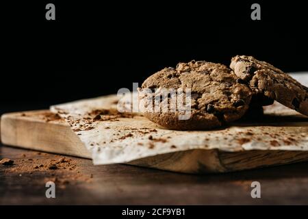 Délicieux biscuits croustillants faits maison avec des chips de chocolat servi sur la pâtisserie papier sur panneau en bois sur fond noir Banque D'Images