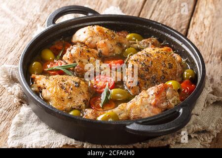 Poulet de cuisine française cuit avec des olives, des tomates et des oignons, des herbes gros plan dans une poêle sur la table. Horizontal Banque D'Images