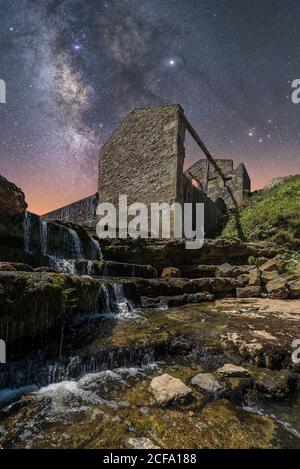 Depuis le dessous de l'ancien château en pierre et petite cascade escaliers dans un ciel sombre avec étoiles et laiteux Banque D'Images