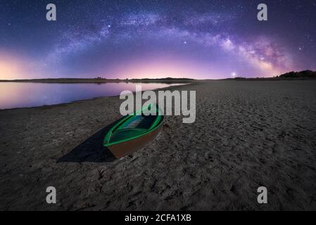 Paysage de sécheresse avec bateau de pêche vert solitaire abandonné sur sec côte du désert sous ciel étoilé coloré de nuit avec laiteux chemin Banque D'Images