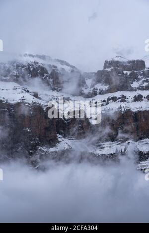 Pics de montagne couverts en partie de neige et entourés de buée brouillard sous ciel nuageux en hiver Banque D'Images