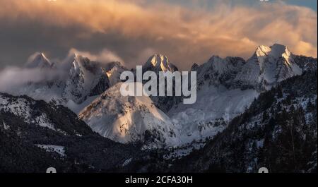 Pics de montagne pointus partiellement couverts de neige et entourés de brouillard sous un ciel pittoresque et nuageux à la tombée de la nuit en hiver Banque D'Images