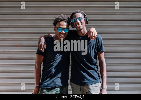 Joyeux jeunes Afro-américains adolescents de sexe masculin dans des lunettes de soleil appréciant passe-temps ensemble en plein soleil dans la rue Banque D'Images