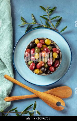 Olives. Une variété d'olives vertes, noires et rouges, avec des feuilles et des cuillères en bois, grenaille de haut en bas Banque D'Images