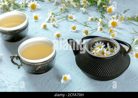 De dessus pot de thé camomille servi sur une tasse rustique avec fleurs fraîches sur fond bleu Banque D'Images