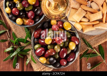 Olives. Une variété d'olives vertes, noires et rouges, avec du vin et des gressins sur un fond rustique en bois, gros plan au plafond Banque D'Images