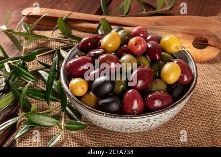 Olives. Une variété d'olives vertes, noires et rouges, un gros plan avec des feuilles sur un fond rustique en bois Banque D'Images
