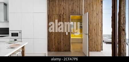 Intérieur de cuisine moderne avec porte en bois et murs blancs dans un appartement minimaliste Banque D'Images