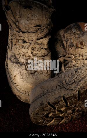 Paire de vieilles bottes de marche recouvertes de boue épaisse et sèche, avec des lumières studio et un tapis de chaussures rugueux. Banque D'Images