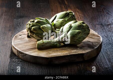 Artichauts verts frais disposés sur une planche à découper en bois sur rustique table de bois Banque D'Images