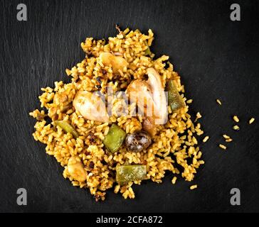 Vue de dessus de paella espagnole épicée appétissante avec poulet et fruits de mer servis sur un tableau en ardoise noire Banque D'Images