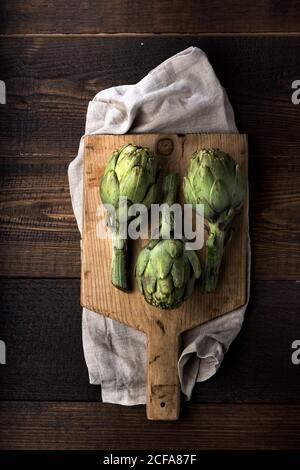 Vue de dessus des artichauts verts frais disposés sur la coupe de bois planche sur table de bois rustique Banque D'Images