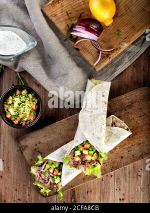 Vue de dessus de l'en-cas turc traditionnel de blé dur fait avec emballé pain plat rempli de kebab avec de la viande d'agneau et des légumes servi sur une table en bois Banque D'Images