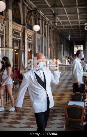 Venise. Italie. Un serveur portant un masque facial pendant la pandémie de Covid-19 livre des boissons au Caffè Florian sur la place Saint-Marc. Banque D'Images