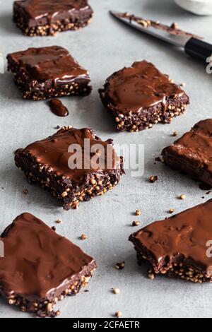 Délicieux biscuits faits maison coupés en carrés et recouverts de glaçage au chocolat noir et graines de quinoa sur parchemin Banque D'Images