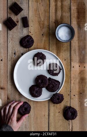 De ce qui précède, les petits gâteaux aromatiques anonymes qui attrapant les mains sont couverts de sirop de chocolat dans une assiette blanche sur une table en bois Banque D'Images