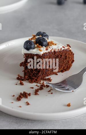 Tranche de gâteau au chocolat maison recouvert de pâte fraîche fouettée crème et bleuets entiers placés sur une table dans une cuisine légère Banque D'Images