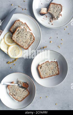 Vue de dessus de savoureux aromatiques citron maison et graines de pavot génoise coupée sur les portions et servie sur des assiettes blanches sur une table en marbre Banque D'Images