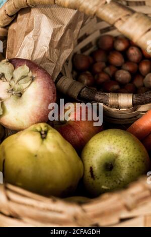 De dessus panier en osier avec légumes mûrs frais colorés et fruits en composition avec herbes et noisettes sur terre parmi les feuillages secs bruns à côté de plaid bleu chaud en automne jardin Banque D'Images