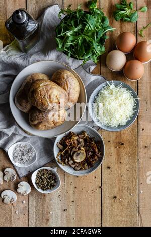 De dessus bols avec pommes de terre farcies aux pommes de terre sautées herbes vertes frites champignons œufs fromage râpé et bouteille d'huile d'olive table en bois Banque D'Images