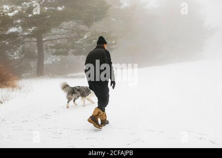Homme âgé et son chien marchant sur une brume enneigée jour sur la forêt Banque D'Images