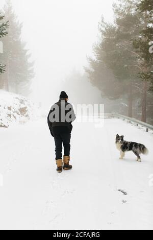 un homme et son chien méconnaissables marchent par une journée brumeuse avec de la neige Banque D'Images