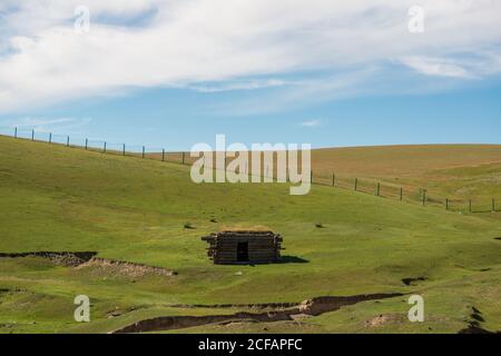 Petite cabine située sur une pente herbeuse et entourée d'une clôture le jour ensoleillé dans la campagne Banque D'Images