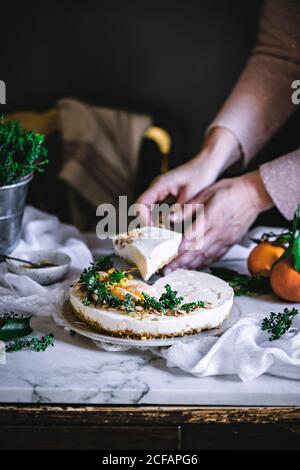 Gâteau blanc crémeux et savoureux à la mandarine, décoré de vert et d'agrumes sur la barre de coupe, couper avec les mains de la cuisinière Banque D'Images