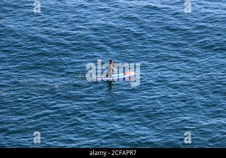 Paddle-boarder solitaire s'agenouillant pagayer en mer au large de Cabo Menor petit cap Santander Cantabria Espagne Banque D'Images