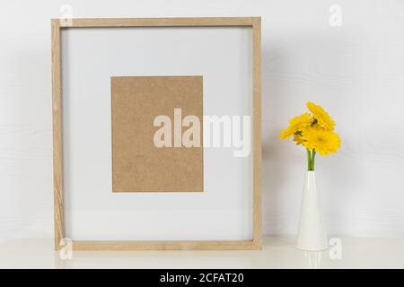 Vue d'un cadre photo, avec des tulipes jaunes placées dans un vase en verre sur fond blanc Uni Banque D'Images
