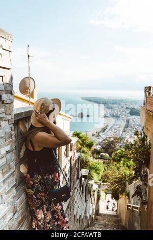 De l'arrière-plan de la femme méconnaissable en tenue d'été prenant photo de paysage marin debout sur les escaliers de pierre de rue au-dessus de la rive Banque D'Images