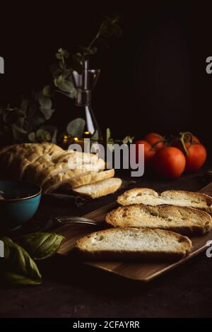 Morceaux de pain frais placés sur la table près des tomates fraîches et feuilles de basilic sur fond noir Banque D'Images