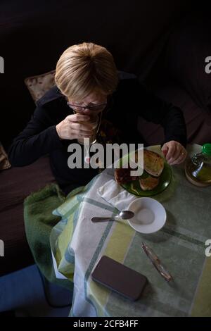 D'en haut, une femme d'âge boit du café du verre au petit déjeuner tout en étant assise à table Banque D'Images