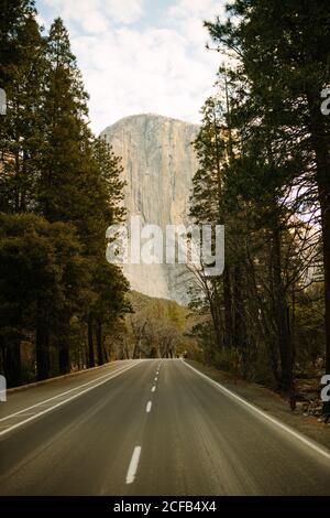 Perspective de la route asphaltée traversant la pittoresque vallée verte entre grands arbres contre ciel nuageux et haute montagne en été En Californie Banque D'Images
