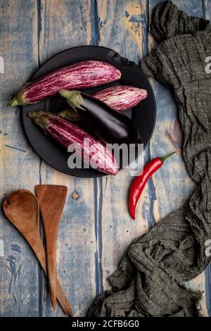 Ensemble d'aubergines fraîches et mûres placées près d'un morceau de rayures tissu sur un plan d'examen en bois abîmé Banque D'Images