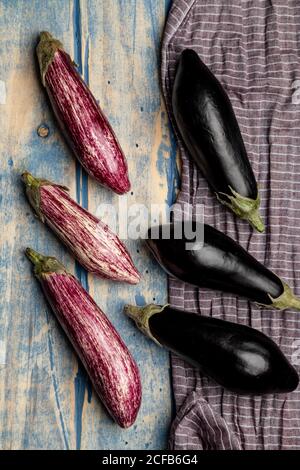 Ensemble d'aubergines fraîches et mûres placées près d'un morceau de rayures tissu sur un plan d'examen en bois abîmé Banque D'Images