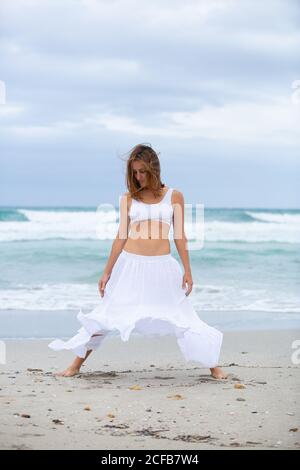 Belle jolie femme en costume blanc dansant sur le sable à proximité la mer Banque D'Images