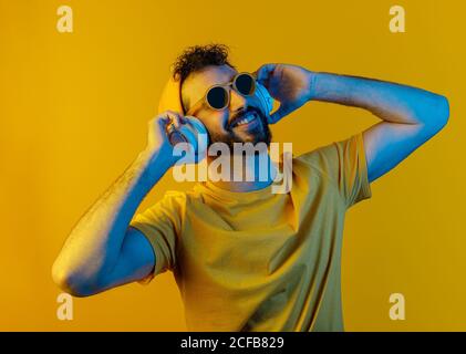Joyeux barbu dans une tenue élégante à l'écoute de la musique un casque blanc contemporain sur fond jaune Banque D'Images