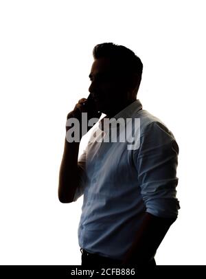 Vue latérale d'un homme confiant en chemise blanche main dans la poche et parler sur un smartphone isolé sur blanc arrière-plan Banque D'Images