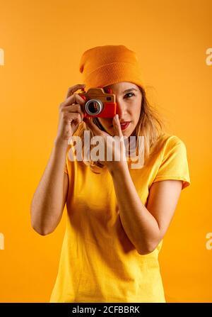 Bonne jeune femme regardant l'appareil photo tout en tenant un faux appareil photo en bois vintage debout sur fond jaune Banque D'Images
