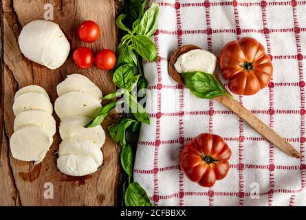 Tomates fraîches et fromage mozzarella avec feuilles de basilic pour la salade placé sur une planche en bois et une serviette en tissu Banque D'Images