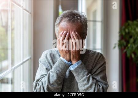 Homme âgé tenant la tête entre les mains dans le désespoir Banque D'Images