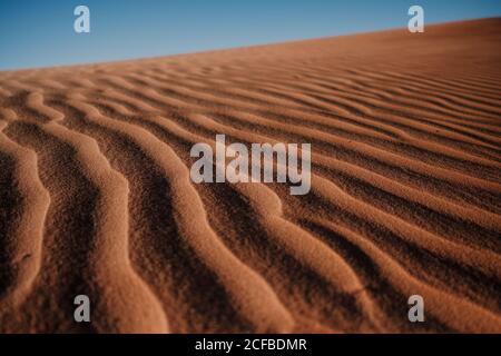 Gros plan surface de sable ondulée sur dune dans désert aride contre Ciel bleu sans nuages au Maroc Banque D'Images