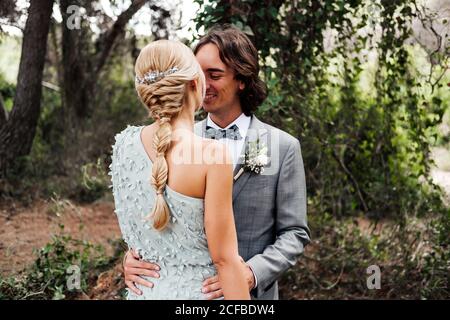 Jeune couple récemment marié dans le port de mariage debout et embrassant sur le chemin entre belle forêt verte avec de grands arbres Banque D'Images