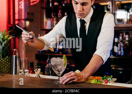 Jeune barman élégant travaillant derrière un comptoir de bar pour mélanger des boissons avec fruits Banque D'Images