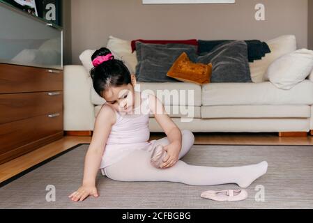 Vue latérale de la jolie fille en léopard et collants assis sur le sol près du canapé et de mettre des chaussures de danse avant répétition de ballet à la maison Banque D'Images