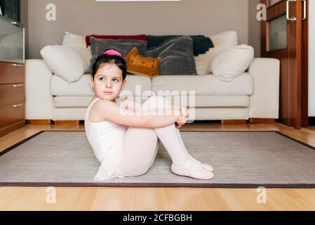 S'ennuient une petite fille pensive en léopard et collants assis dessus le sol est loin de vous reposer pendant la répétition du ballet à la maison Banque D'Images